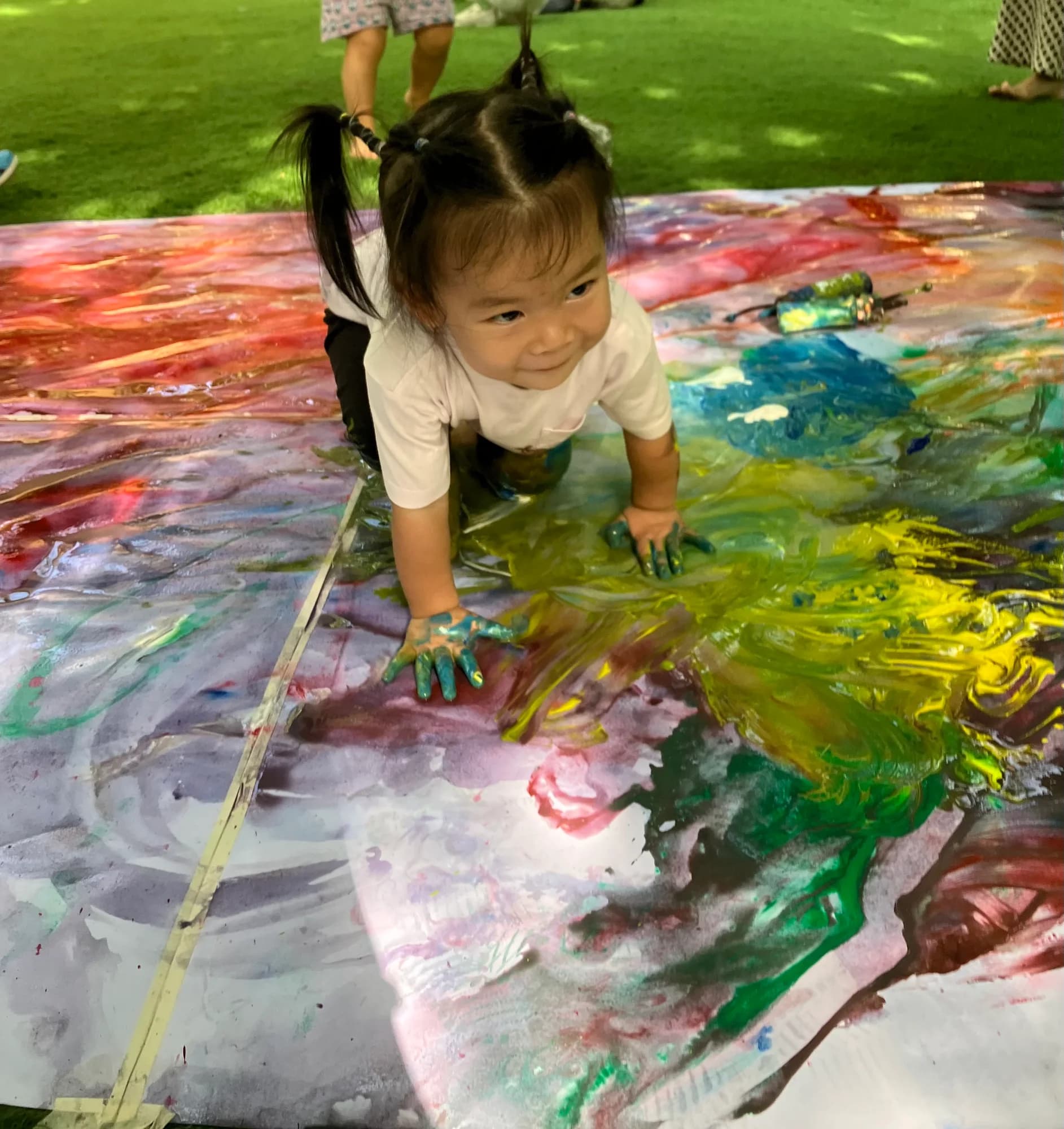 A young child exploring colourful paint with their hands outdoors